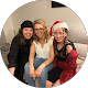 Three smiling girls sitting together, one wearing a Santa hat
